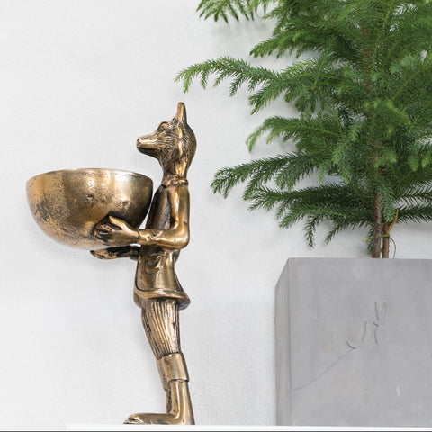 Bronze statue of a figure holding a bowl next to a potted plant on a white background