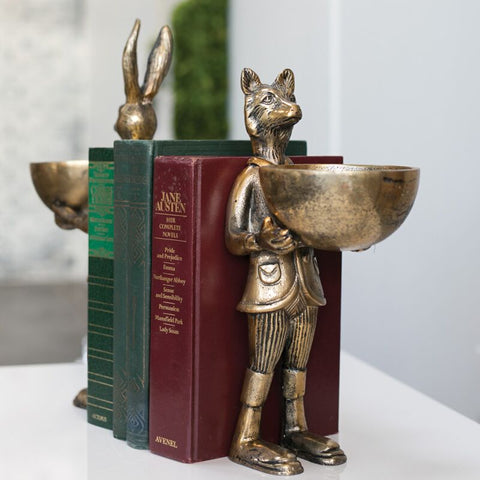 Decorative bookends shaped like a fox and a rabbit holding books on a white surface.