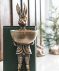 Decorative figure of a rabbit in a suit holding a bowl on a white surface.