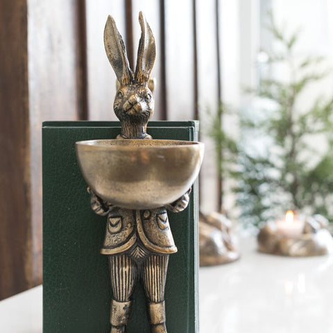 Decorative figure of a rabbit in a suit holding a bowl on a white surface.