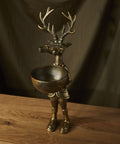 Bronze deer figurine with a bowl on a wooden surface and dark curtain background