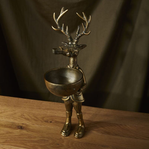 Bronze deer figurine with a bowl on a wooden surface and dark curtain background
