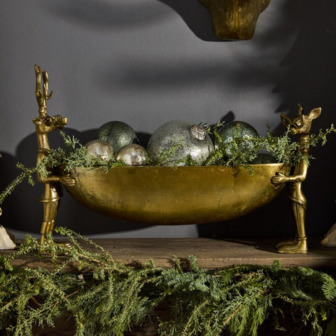 Decorative setup with a gold bowl, silver balls, and greenery on a dark background