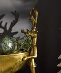 Gold figurine of a person with antlers holding a bowl with greenery against a dark background