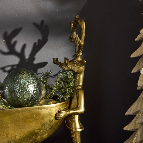 Gold figurine of a person with antlers holding a bowl with greenery against a dark background