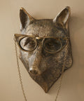Bronze fox head with glasses and chain on a beige wall