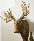 Decorative gold deer head mounted on a wall with greenery and a pot below.