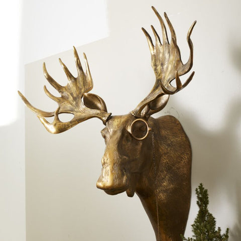 Decorative gold deer head mounted on a wall with greenery and a pot below.