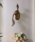 Decorative peacock wall sculpture on a plain wall with a small table and flowers.