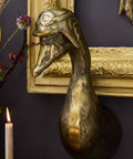 Decorative gold duck head sculpture on a dark wall with a candle and decorative branches.