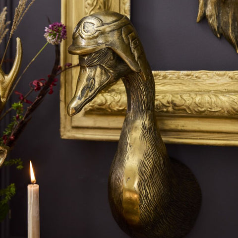 Decorative gold duck head sculpture on a dark wall with a candle and decorative branches.