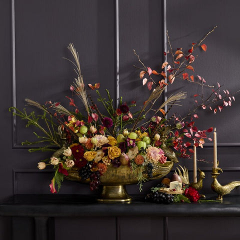 Decorative floral arrangement on a dark surface with candles against a dark background