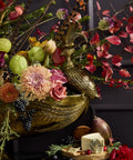 Decorative floral arrangement with a gold urn and fruits on a dark background