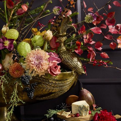 Decorative floral arrangement with a gold urn and fruits on a dark background