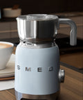 White SMEG coffee machine on a kitchen counter with a cup of coffee and toaster in the background.
