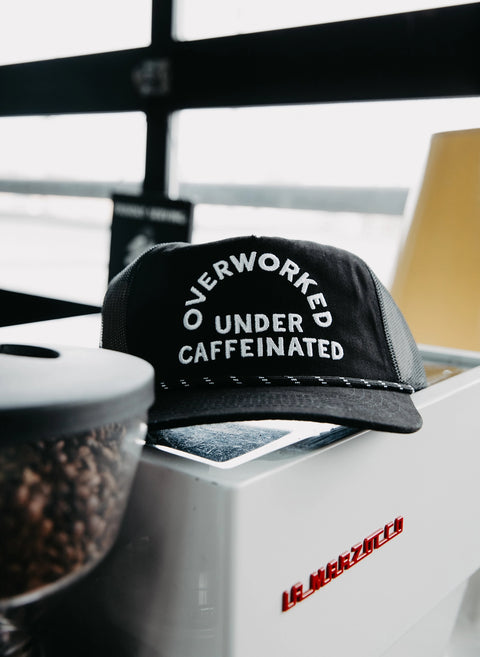 Overworked Under Caffeinated Trucker Hat by Pyknic