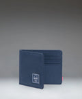 A navy blue bifold wallet with a small white brand patch on the front, standing open to show card slots on the inside, photographed against a dark gray gradient studio background.