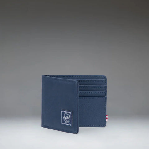 A navy blue bifold wallet with a small white brand patch on the front, standing open to show card slots on the inside, photographed against a dark gray gradient studio background.