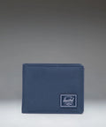 A navy blue bifold wallet with a white Herschel logo patch on the front, set against a dark gray gradient background.