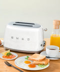 Kitchen scene with Smeg toaster and kettle on a wooden table with breakfast items.