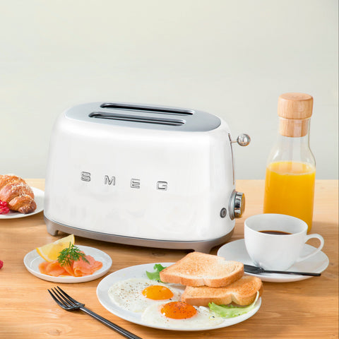 Kitchen scene with Smeg toaster and kettle on a wooden table with breakfast items.