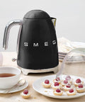 Black Smeg kettle on a wooden table with tea and pastries.