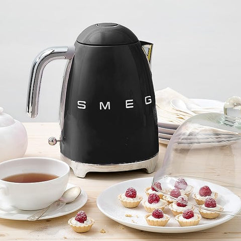 Black Smeg kettle on a wooden table with tea and pastries.