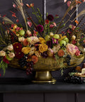 Decorative floral arrangement in a gold bowl on a dark surface with a dark background