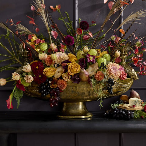 Decorative floral arrangement in a gold bowl on a dark surface with a dark background