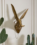 Gold rabbit head sculpture on a wall with potted plants below