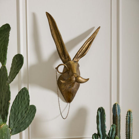 Gold rabbit head sculpture on a wall with potted plants below