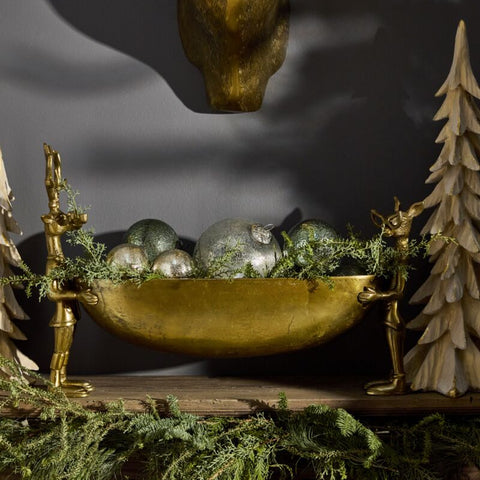 Decorative setup with gold bowl, silver ornaments, and greenery on a dark background