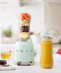 Smeg blender with ingredients and a smoothie on a kitchen counter